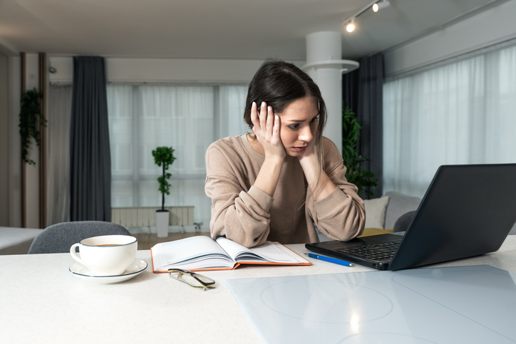 Young stressed and frustrated college student woman sitting at home waiting to her old laptop start to work. Female business person feeling tired from broken computer because she cant work.