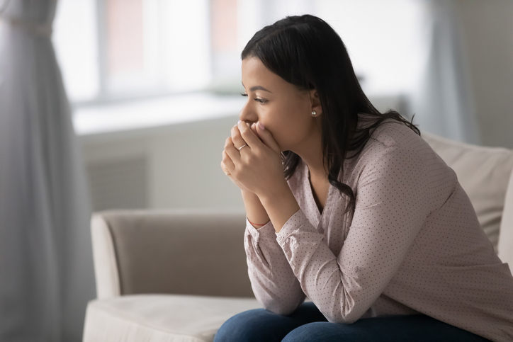 Pensive worried mixed race woman sitting on couch at home