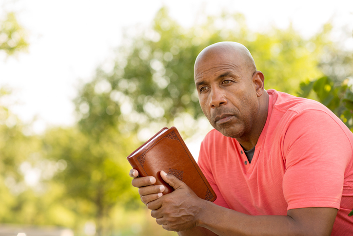 African American man praying and reading the Bible.