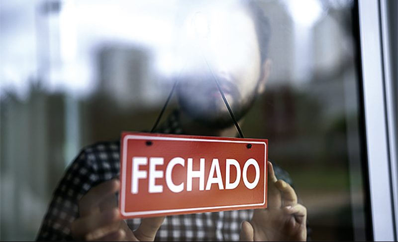 Business owner turning as closed (fechado in portuguese) for business sign in their storefront window