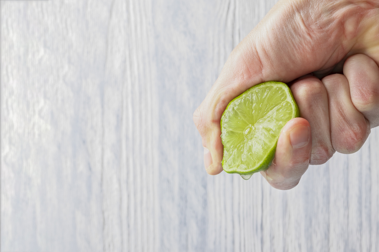 The hand of a man squeezes the juice from a slice of lime half. Juicy drop hanging down.