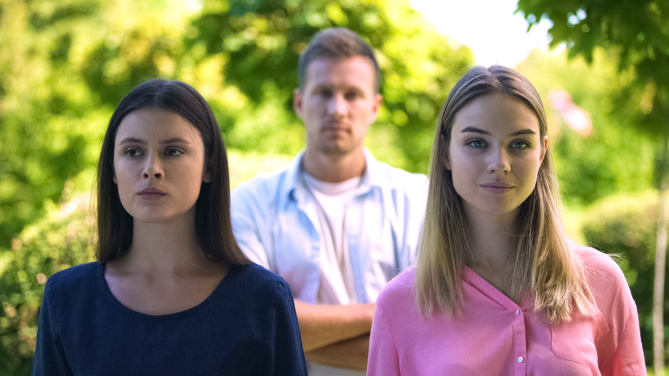 Brunette and blond females with man on background, relations conflict, jealousy