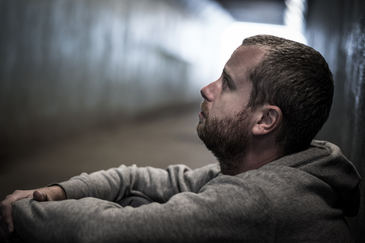 Homeless adult male sitting in subway tunnel begging for money