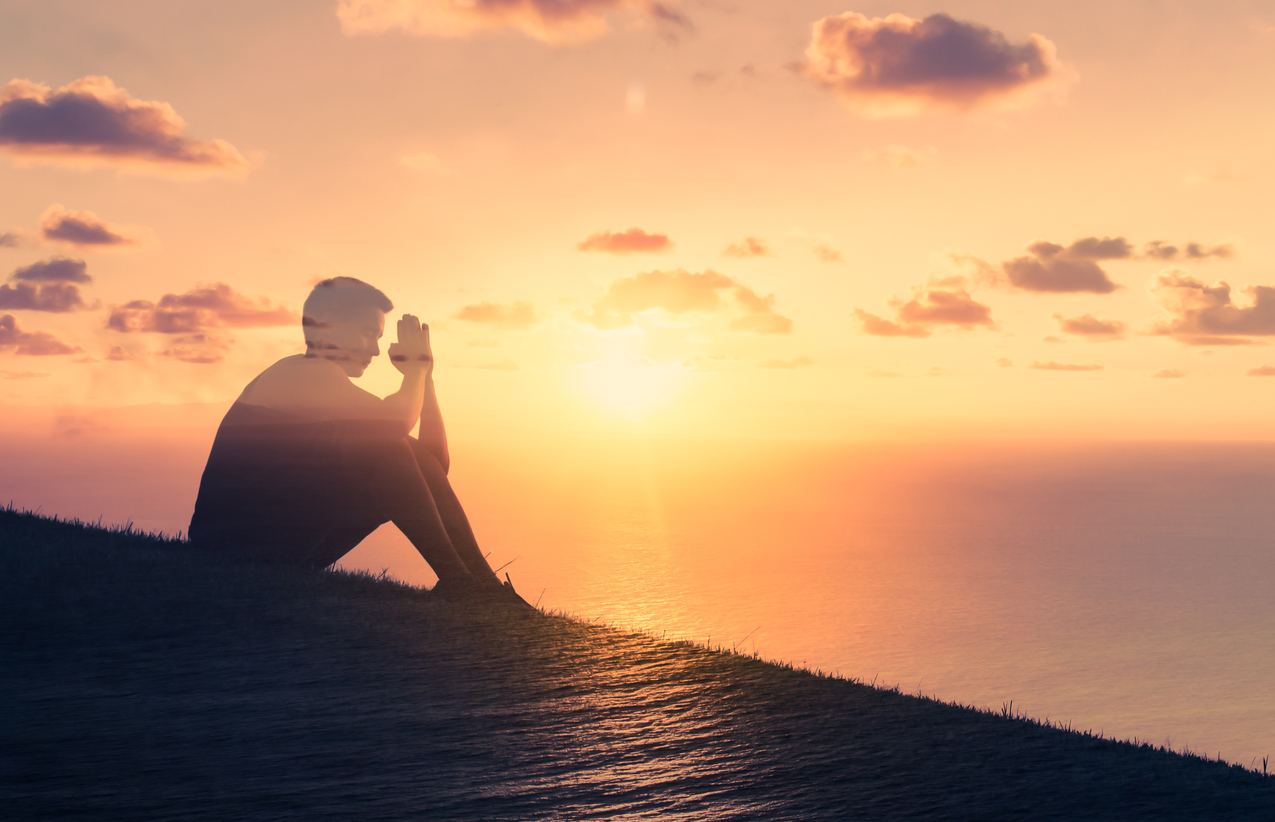 Man making praying hands in a beautiful sunrise setting.