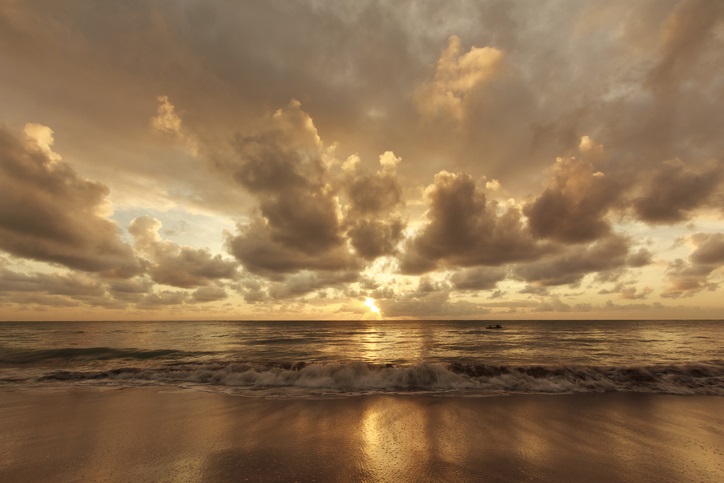 Sun rising on the horizon over water under a dramatic cloudy sky in São Miguel dos Milagres, Alagoas, Northeastern Brazil