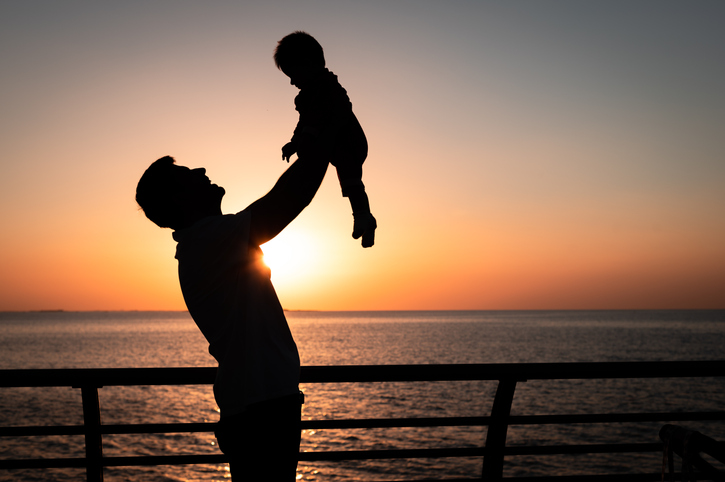 Man holding his baby boy by the seaside at sunset on a summer vacation silhouette