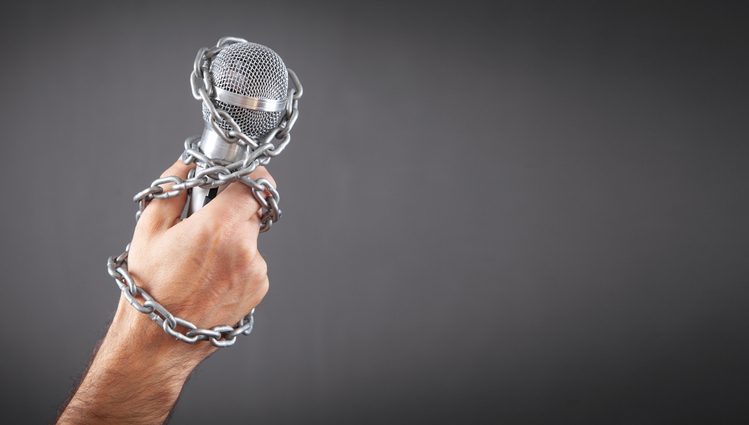 Human hand holding microphone tied with chains.