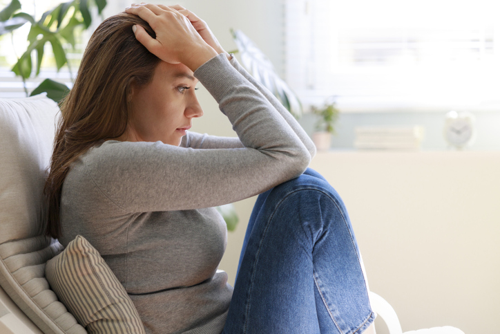 Upset young woman sitting on couch alone at home