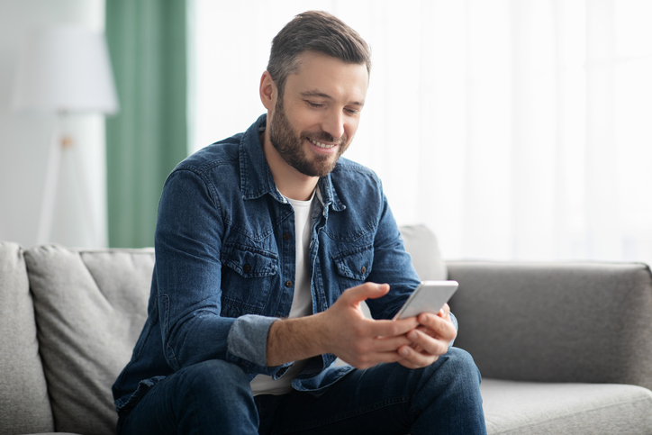 Cheerful middle-aged man sitting on sofa with mobile phone