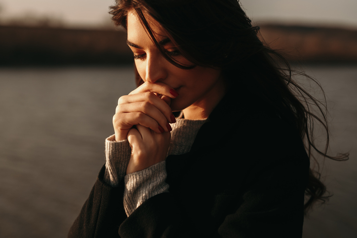 Thoughtful woman standing near lake at sunset