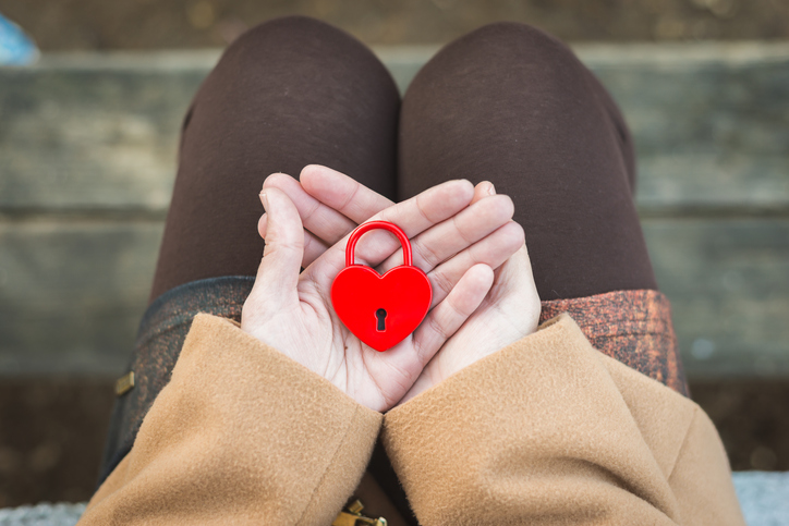 Female hand holds closed red padlock in heart shape