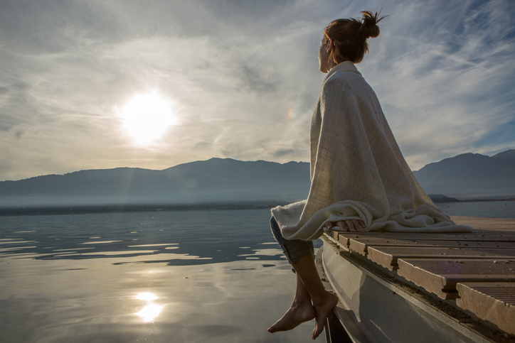 Young woman relaxes on lake pier with blanket, watches sunset