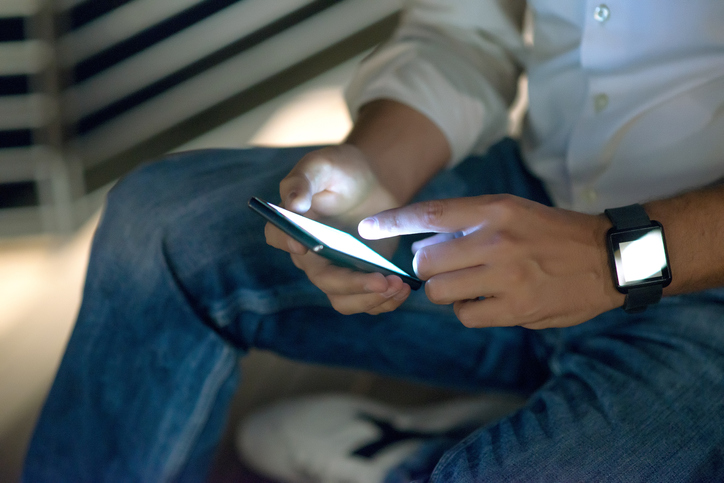 Hands holding smartphone at night wearing smartwatch