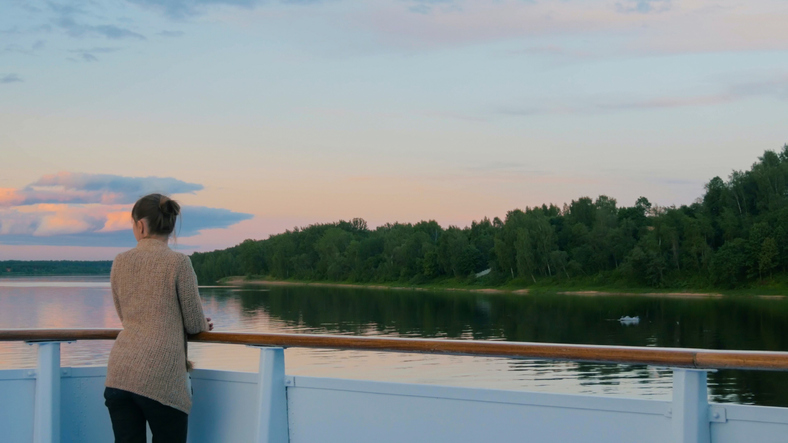 Woman admiring landscape from deck of cruise ship after sunset