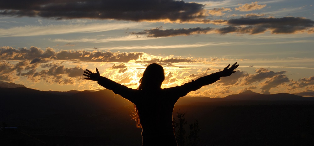 A silhouette of a woman with her arms open in the sunset