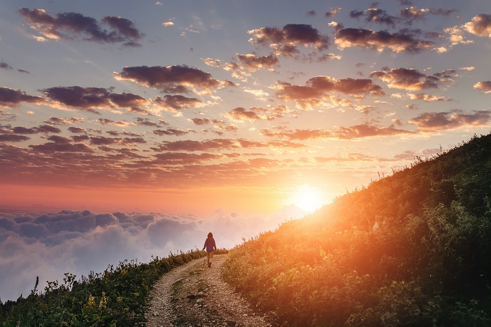 Woman on trail admiring the sunset with clouds and fog.