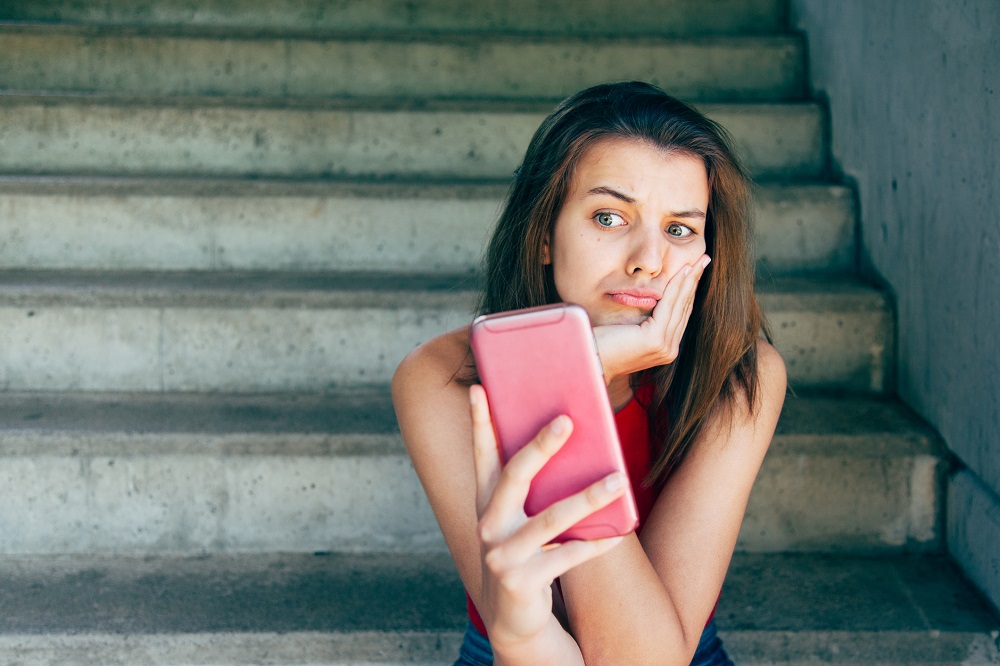 Displeased teen girl looking at her smartphone