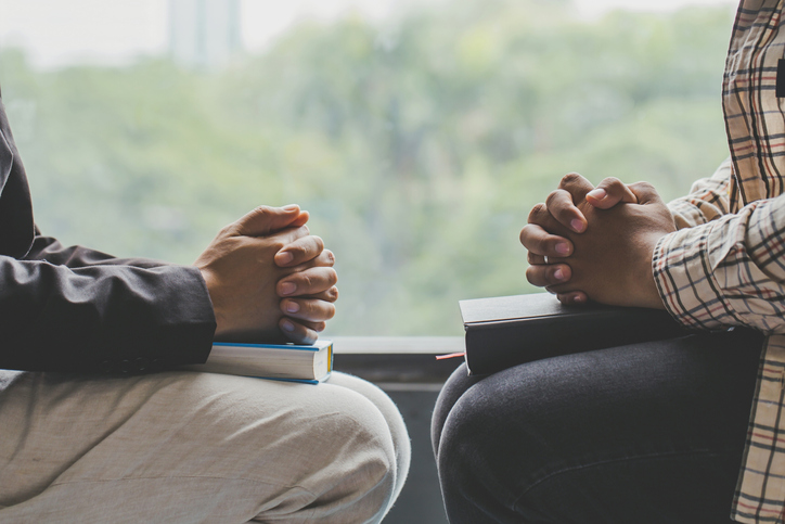 Two man sit on wooden chair while praying to God together in home office with window light,Christian background