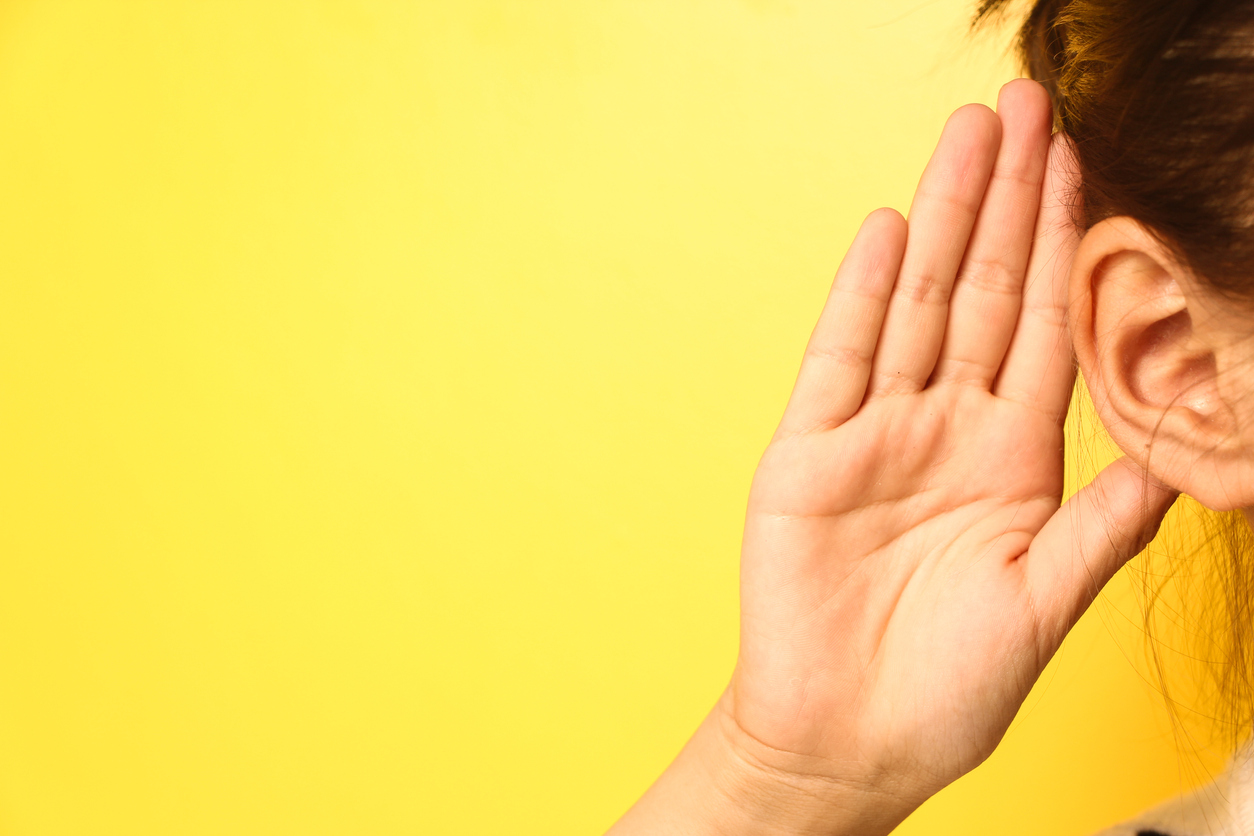 Girl holds her hand near ear and listens carefully isolated on wall