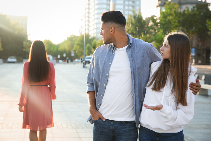 Disloyal man looking at another woman while walking with his girlfriend outdoors