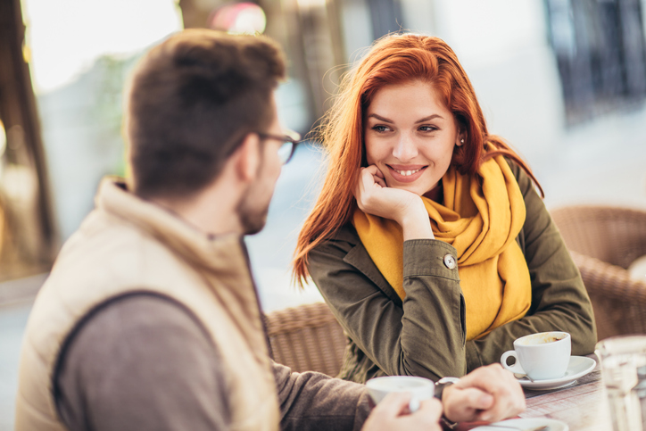 Attractive young couple in love sitting at the cafe table outdoors, drinking coffee