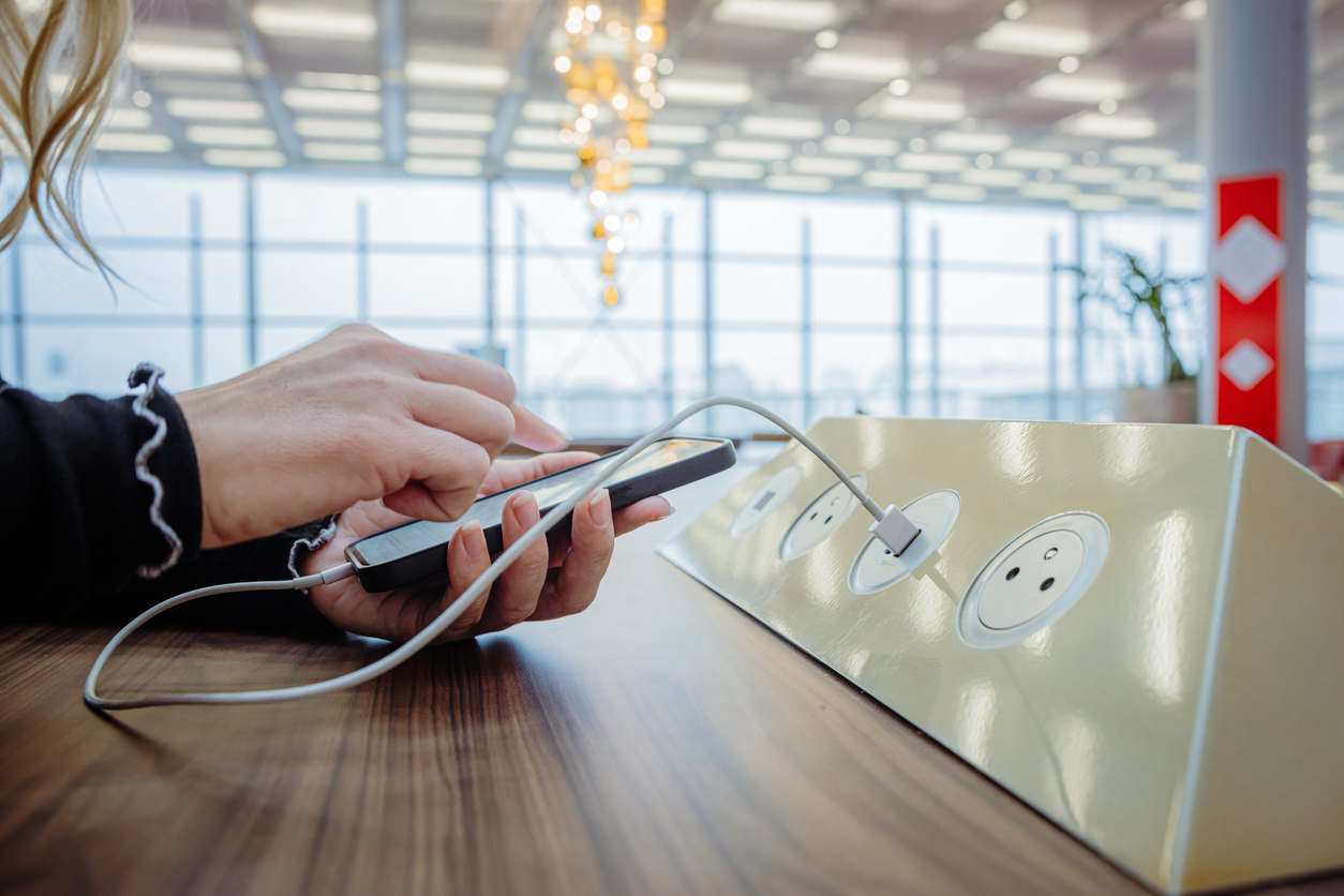Close-up of a oman using her phone while charging it on a charging station in an airport terminal