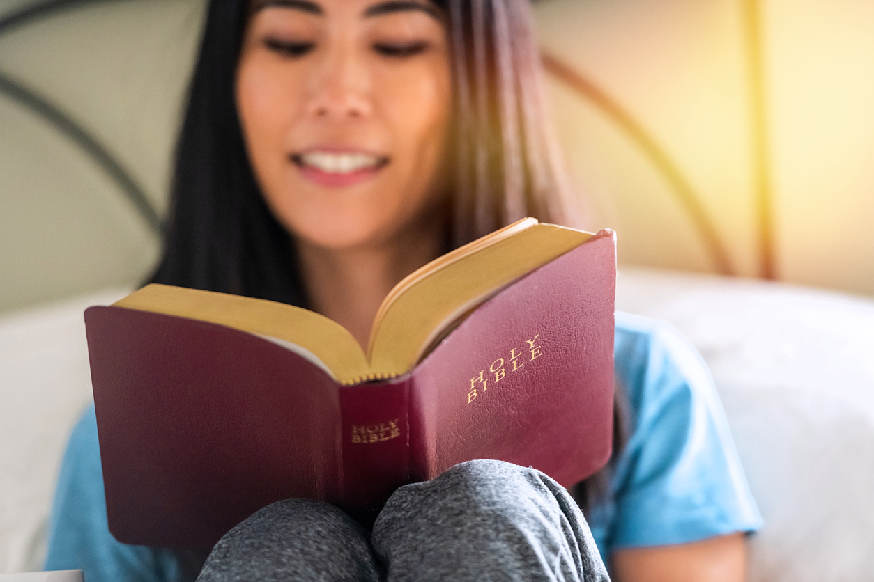 Smiling East Asian woman reading the Bible at home