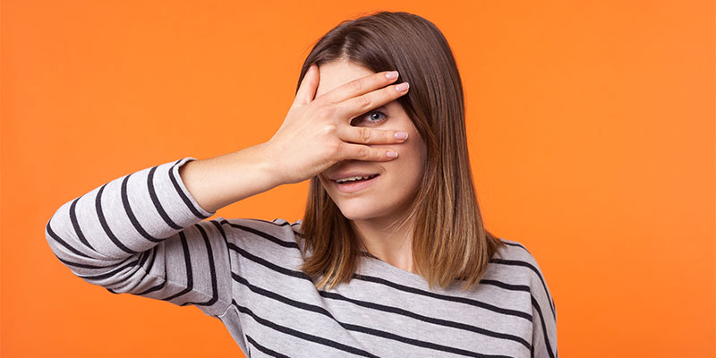 Portrait of curious cheerful woman with brown hair in long sleeve striped shirt. indoor studio shot isolated on orange background