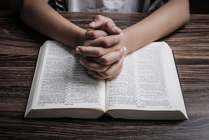 Praying hands with opened holy bible on the wooden desk