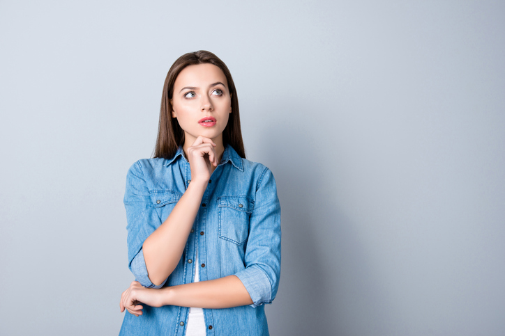 Close up portrait of pretty confident thoughtful girl, holding hand near the face, looking seriously up, standing over grey background with copy space