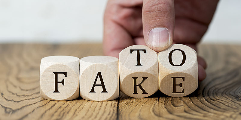 hand is turning two of four cubes, changing the word FACT to FAKE