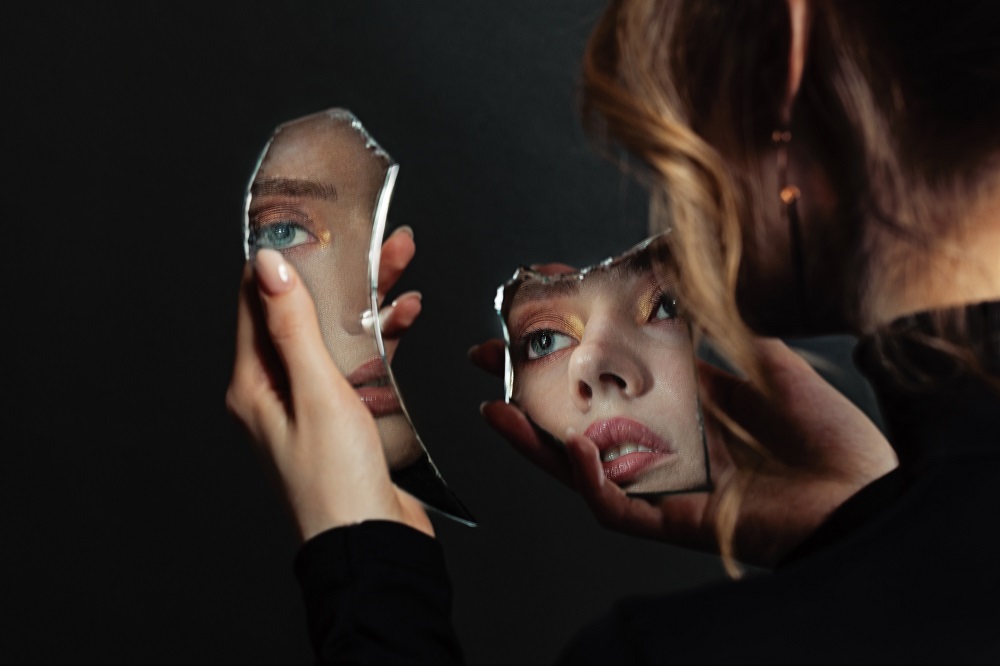 Perfect woman looking at broken self-image mirror on black background