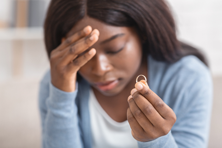 Upset black girl holding gold wedding ring, depressed about divorce