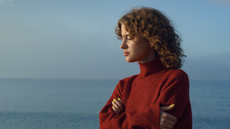 Pensive girl standing at seaside. Thoughtful woman face with closed eyes