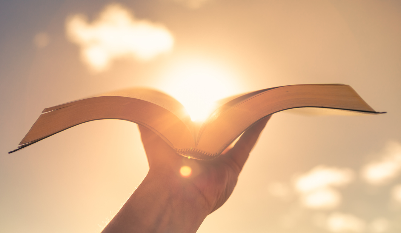 Man holding bible against a sunset sky