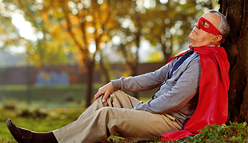 Senior in superhero outfit leaning on tree