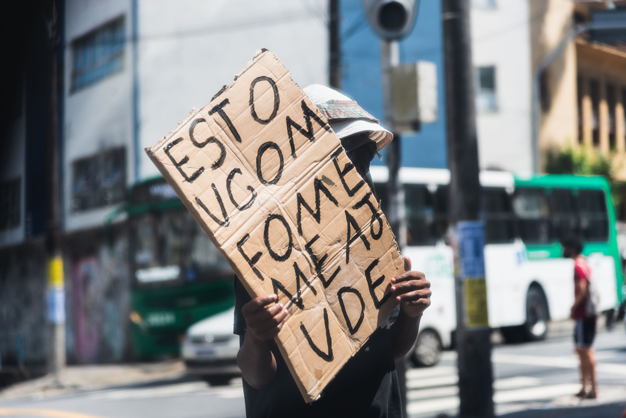 a homeless person holding a cardboard piece with a message