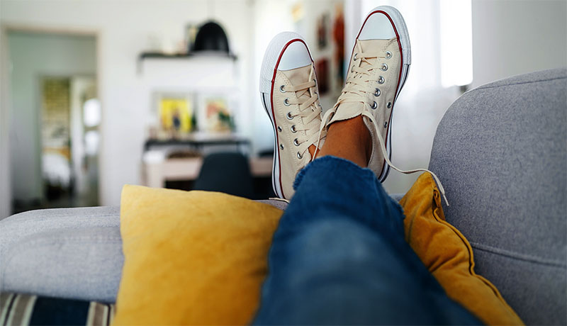Young female lying in new beige sneaker son cozy comfortable living room sofa putting feet on pillows and resting and relaxing. Comfortable clothing and footwear concept