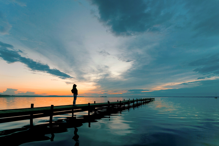 Silhouette of Woman on Lakeside Jetty with majestic Sunset Cloudscape