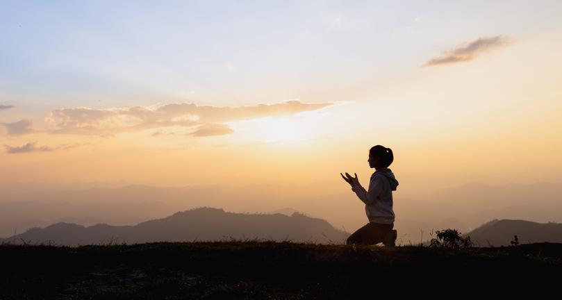 Silhouette of a woman praying outside at beautiful landscape at the top of the mountain, Copy space of man rise hand up on top of mountain and sunset sky abstract background.