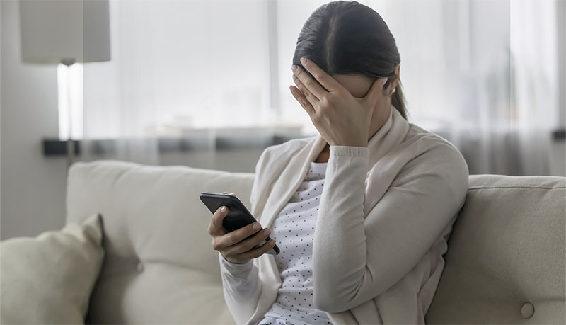 Stressed woman holding smartphone feels humiliated, cyberbullying concept
