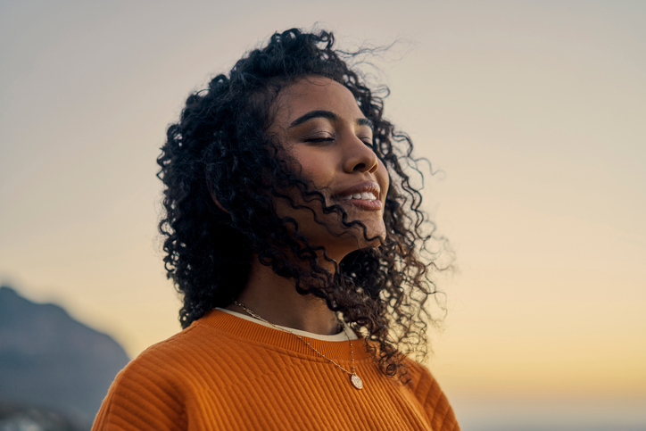 Happy woman in nature, sunset sky peace and smile breathing co2. Wellness beauty, clear outdoor sky andfresh wave of calm. Eyes closed, asthma treatment air and girl with curly hair relaxed face.