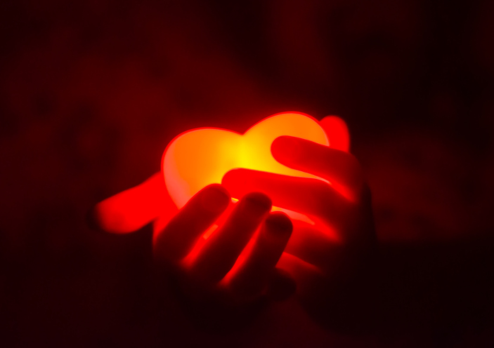 Human hands holding red glowing heart in the dark