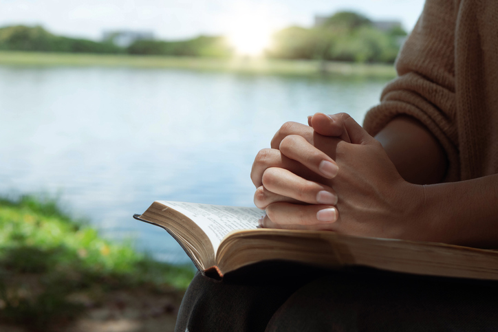 Woman hands praying with a bible in his legs Outdoors