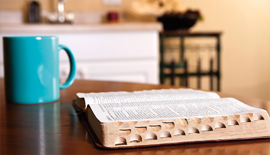 Open Bible on kitchen table with coffee mug