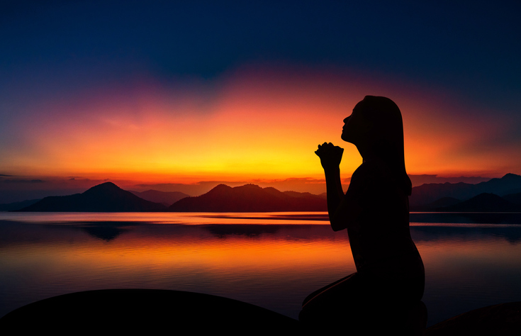 Silhouette of woman kneeling and praying over beautiful sunset