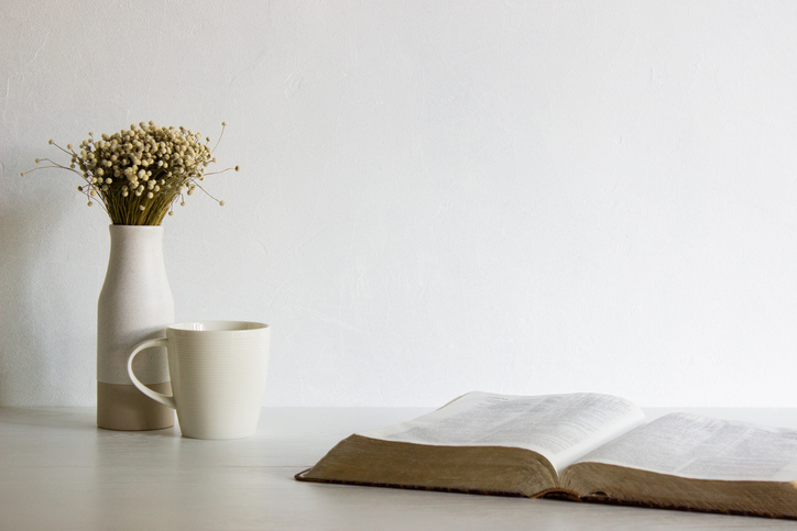 Holy Bible with flower in a vase with coffee cup over the white table.