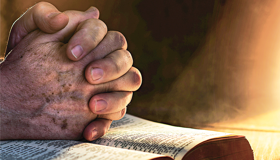 Close up of hands clasped on open Bible