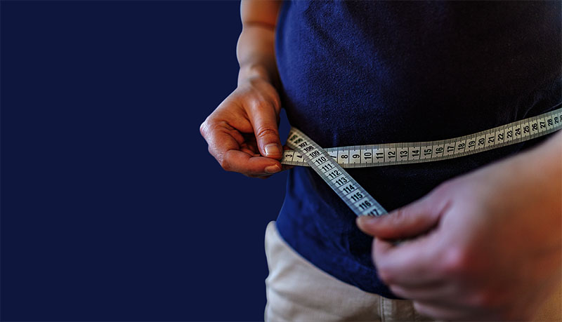 man measures her abdomen with a measuring tape