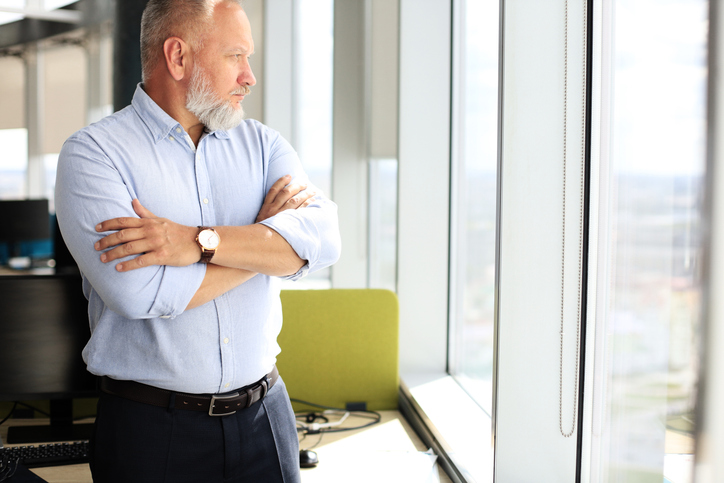 Thoughtful mature business man in a corporate suit looking away while standing near the window.